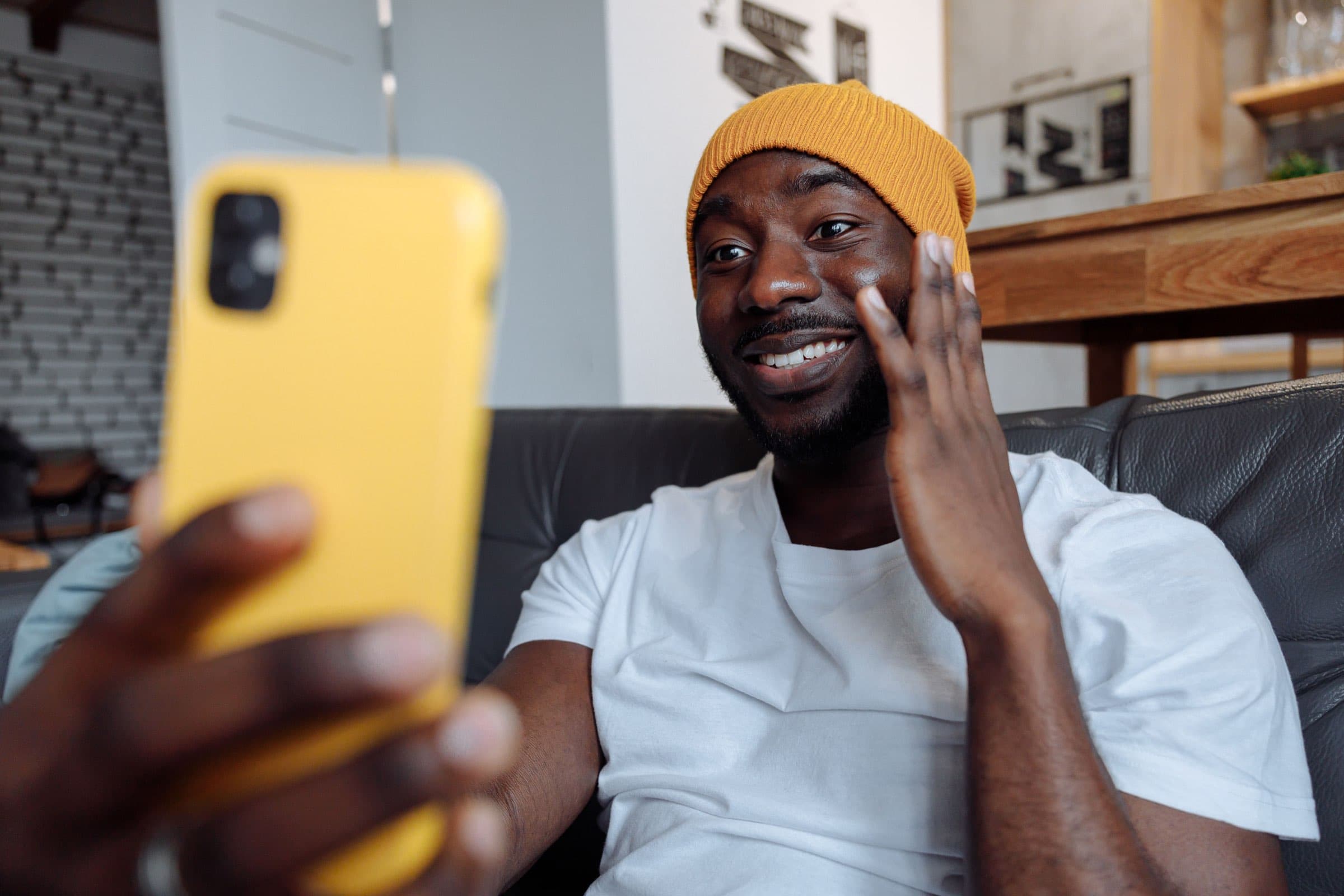 A smiling man on a sofa waving at his phone during a video call